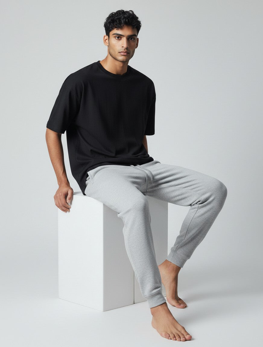 CosmoOtaku unisex grey melange joggers in 260 GSM cotton with a tapered fit and ribbed cuffs worn by a seated model