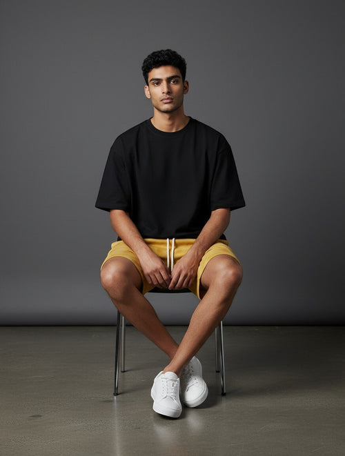 CosmoOtaku mustard yellow drawstring shorts worn by a man in a black t-shirt and white sneakers on a grey background